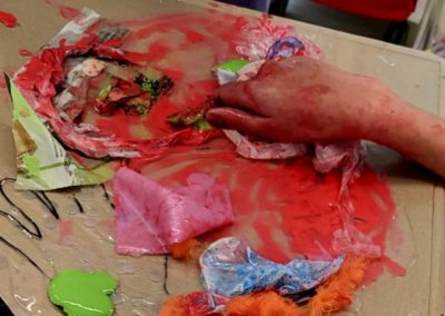 Kind arbeitet mit Stoff, Papier, Leim und Farbe auf Glas